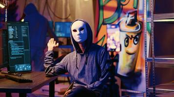 Masked hackers filming ransom in hidden underground base, threatening to release stolen data publicly if payout demands are not met. Rogue programmers using phone to record blackmail footage photo