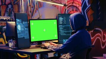 Hackers using green screen PC to code malware designed to exploit network backdoors. Cybercriminals use mockup monitor while bypassing security measures in graffiti painted bunker photo
