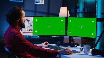Photographer using photo editing software on Chroma key multi monitors setup to improve images quality. Photo editor utilizing pictures retouching application on green screen display