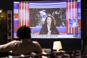 Cord cutter sitting on couch in front of widescreen smart TV displaying streamed news program. Person watching big television screen showing on demand channel with newscast coverage photo
