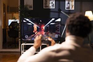 Player using controller to play first person shooter videogame on smart TV, enjoying leisure time. Man in home theatre using high tech gaming console joystick to destroy flying robots photo