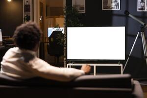 Person using isolated screen TV to binge series on subscription based streaming services. Cord cutter relaxing on couch, enjoying on demand shows on mockup television set photo