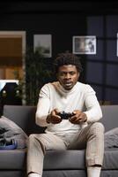 African american player using controller to play videogames on smart TV, enjoying leisure time in living room. Man in home theatre using gaming console joystick to complete levels in singleplayer game photo