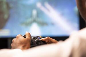 Close up of controller held in gamer hands playing classic arcade action videogame on ultrawide smart TV, flying through space debris. Man using high tech gaming console gamepad photo