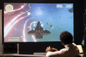 Man playing galaxy flying videogame on large smart TV, relaxing. Competitive gamer having fun on gaming console in stylish apartment living room, piloting spacecraft using gamepad photo