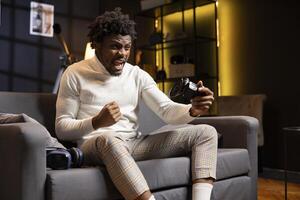 Excited gamer screaming from joy after winning gaming console game in living room. Cheerful player bragging after being victorious in videogame, defeating all enemies using controller photo