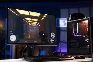 FPS videogame left open on PC screen in empty neon illuminated apartment living room. Shooter game on computer desktop display in RGB lit home late at night with no people in photo