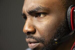 African american gamer feeling sad after losing online multiplayer action videogame match while talking on headphones with teammates. Close up shot of dejected man at game over message on monitor photo