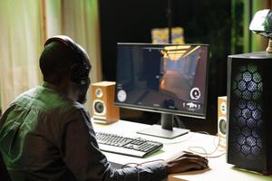Man in dark living room playing science fiction videogame on gaming PC, concentrating on shooting foes. Gamer battling flying robots with futuristic gun in online singleplayer shooter photo