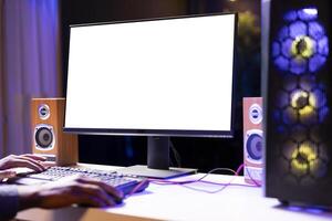 Man in dimly lit apartment playing games on isolated screen gaming PC at computer desk, enjoying day off from work. Gamer battling enemies in online multiplayer shooter on mockup monitor photo