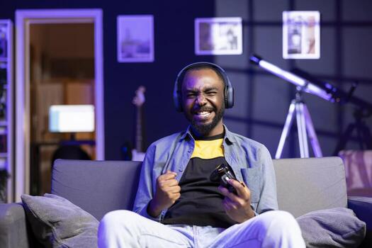 Portrait of euphoric player wearing headphones, celebrating after being victorious in multiplayer videogame. Gamer throws fists in air from excitement after winning game on console system with gamepad photo