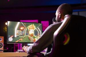Man in neon lit apartment playing immersive games on gaming PC at computer desk, unwinding after work. Gamer competing against enemies in internet multiplayer shooter photo