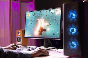 African american man playing SF space videogame on PC screen, shooting asteroids. Gamer enjoying spaceship flying game on computer desktop display, navigating through meteorites photo