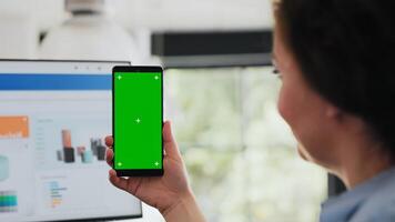 Woman holds smartphone at desk, checking isolated greenscreen template presented on mobile device. Business manager working with modern layout technology, chromakey copyspace. Close up. photo
