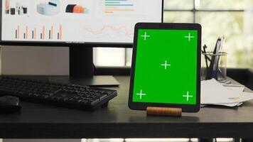 Desk with greenscreen on modern tablet in business coworking space, showing isolated chromakey layout design on mobile gadget display. Empty office workstation running device with copyspace. photo