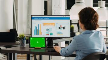 Business manager checks greenscreen and works on problem solving, analyzing blank copyspace mockup template and small agency sales network. Person at office desk with tablet and pc. photo