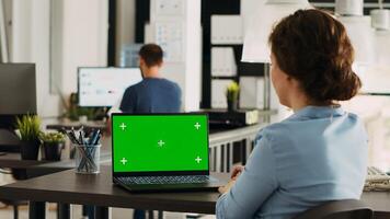 Team leader analyzes greenscreen display on laptop, working on business operations in open floor plan office. Employee using portable computer with blank mockup copyspace on pc. photo
