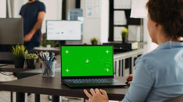 Manager working at office desk with greenscreen on laptop, analyzing mockup chromakey display and isolated copyspace template. Woman using personal computer at workstation. photo
