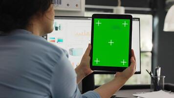 Office worker examines greenscreen layout in coworking space, working on business operations and looking at isolated chromakey display. Woman holding tablet with blank copyspace. photo
