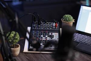 Professional podcasting setup with laptop, modern audio mixer and numerous buttons for dynamic recording experience in home studio. Image showing electronic gadgets used for live streaming talk shows photo
