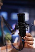 Detailed view of black individual using a professional microphone for broadcasting a live radio show in home studio. Closeup shot of african american person touching a modern mic used for recording. photo