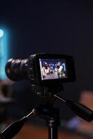 Detailed view of professional camera recording male journalist with notebook interviewing famous blogger. Selective focus of digital device on tripod filming black couple doing live talk show. photo