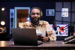 Black male blogger carrying a notebook and gazing at camera, discussing multiple topics with his online audience. African American influencer creates content by reading an outline from a book. photo