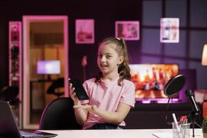 Smiling child filming assessing smartphone performance, talking about components used. Gen Z media star shoots mobile phone review for online channel, pleased with high quality materials photo