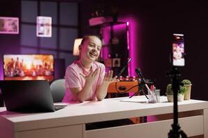 Laughing child having fun doing content creation using selfie camera to film vlog channel intro. Kid presenting today topic in pink neon illuminated living room used as vlogging studio photo