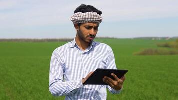 Young indian farmer working in a wheat field, inspecting and tuning irrigation center pivot sprinkler system on tablet video