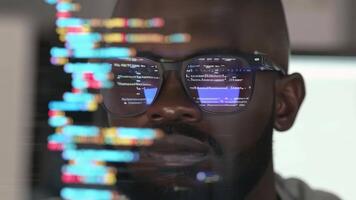 Focused programmer with eyeglasses reflecting code on screen, analyzing complex data for software development in a high-tech environment. video