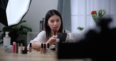 Footage of Beautiful asian woman blogger is showing how to makeup and use cosmetics. In front of the camera to record vlog video live streaming at home. Influencer and cosmetics concepts.