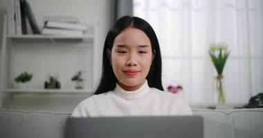Footage of Happy young Asian woman using a laptop computer while lying on the sofa in the living room. Wellness at home, relaxing and lifestyle concepts. video