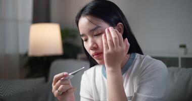 Footage steady shot, Unwell young woman have a fever and measure temperature with a thermometer while sitting on sofa in the living room at home, healthcare woes video