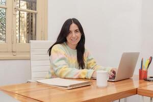Portrait of a smiling young woman working on laptop computer at home photo