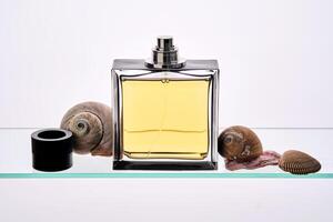 A bottle of perfume in yellow on a glass shelf with seashells in a marine style. photo