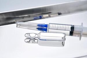 Syringes with needles and an ampoule in a stainless steel medical tray. photo