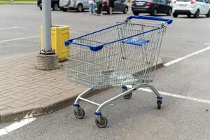 A shopping cart sits on the pavement, near a light pole, in a parking lot photo