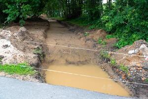 Construction site with muddy puddle, dirt path, hill, forest on right photo