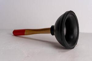 A plunger with a black rubber cup and a wooden handle with a red tip photo