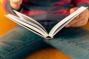 Unrecognizable inquisitive boy immersed in book reading while sitting on the couch photo