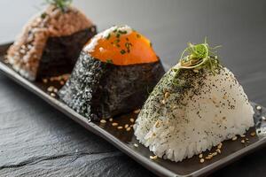 Three onigiri, a Japanese rice ball, are presented on a black plate photo