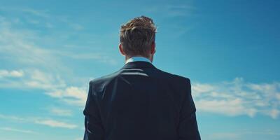 Rear view of a businessman in a suit looking at the sky on a sunny day, symbolizing ambition and future. photo
