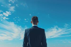 A businessman in a suit gazes at a pristine blue skyline, reflecting ambition, possibility, and future objectives photo