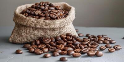 Roasted coffee beans have spilled from a burlap sack onto a grey surface, creating a rich and aromatic scene photo