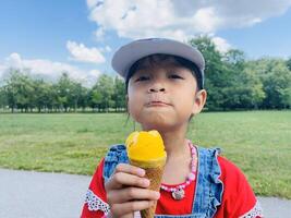 A five years old Asian child eats ice cream in the summer when it's hot outside. Mango Ice cream in a waffle cone. A happy and contented child in the park photo