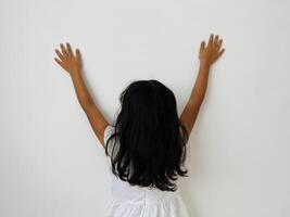 A five years old Asian child with long hair facing away from the camera with both hands raised upwards, copy space for text and advertisement photo