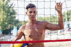 portrait of volleyball player standing in front of net at beach photo