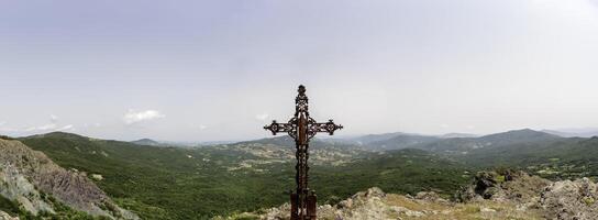 closeup of a rusty metal cross in front of a landscape of the hills photo