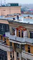 Building of a new tower house. Workers on the roof of multistorey building during the construction on the cityscape. Aerial view. Vertical video
